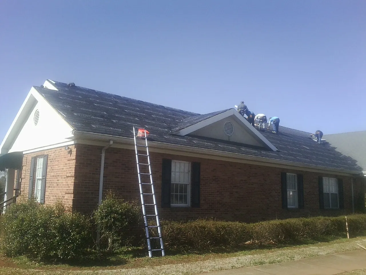 Crew tearing shingles off a brick ranch roof with a ladder set — Emergency Roof Repair work by our crew in South Bethlehem