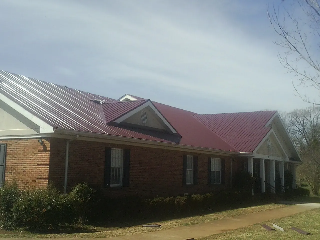 Red metal roof with gabled entries on a long brick building, from a Hail Damage Roof Repair job in South Bethlehem