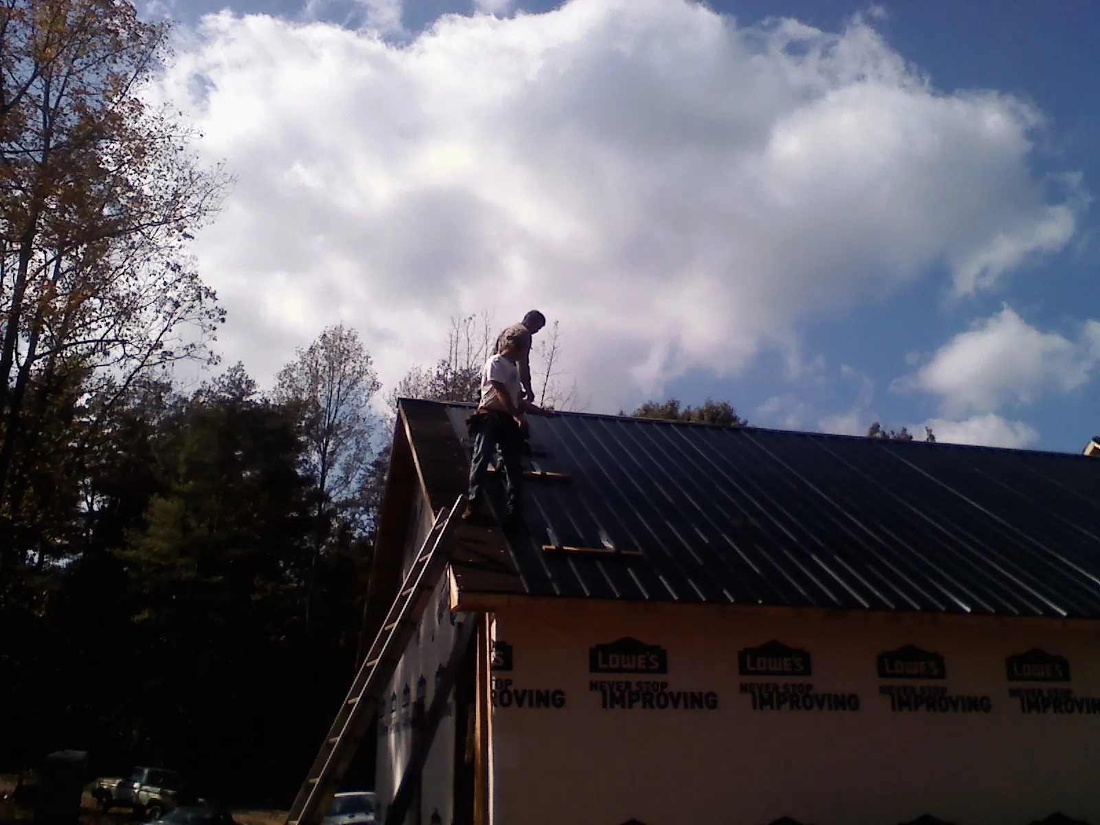 Roofer fastening dark metal panels high against a cloudy sky, from a Roof Inspection job in South Bethlehem
