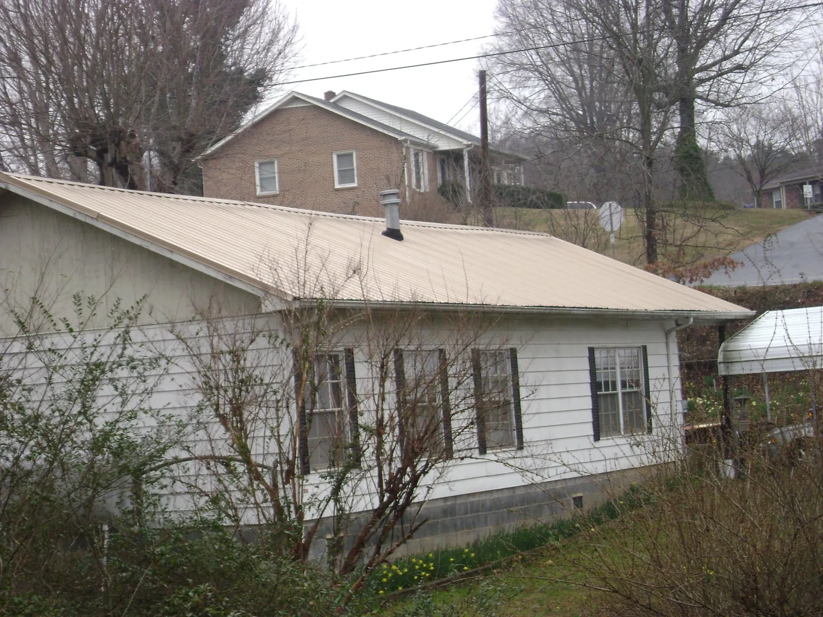 Tan metal roof on a white sided house set into a hillside — Commercial Roofing by Roofing Brothers in South Bethlehem